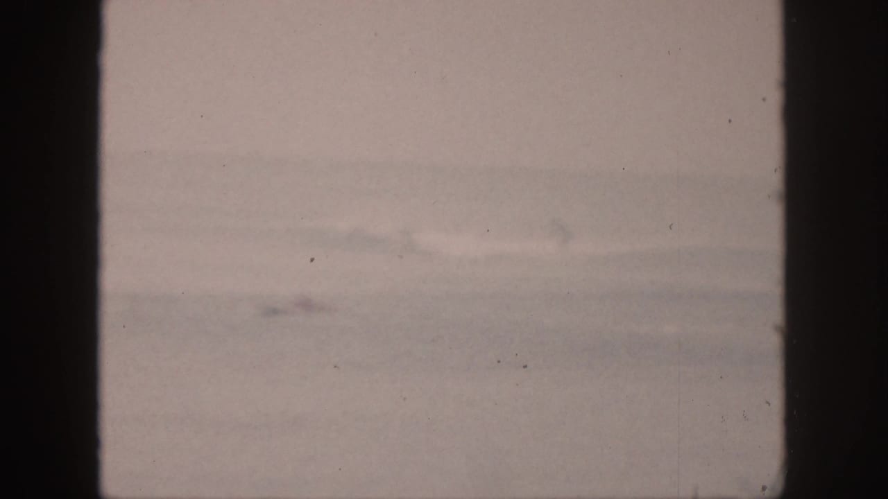 Soft, pale ocean view with faint surf line and film scratches.