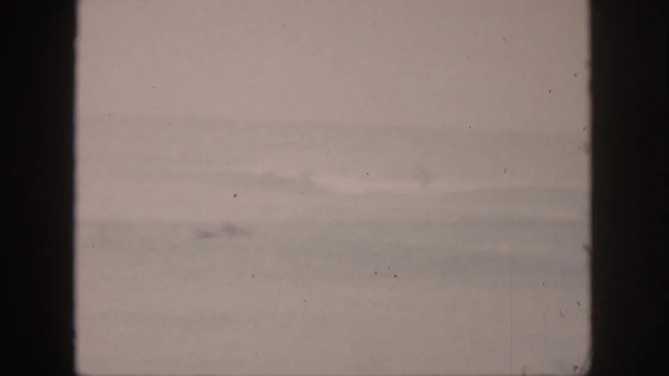 Faded 8mm view of Hawaii surf, with distant wave activity softened by haze and age marks.