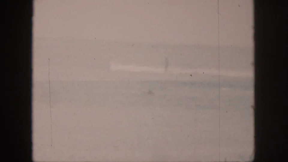 1959 Hawaii home-movie frame of shallow nearshore water with a low wave band and faded 8mm color.