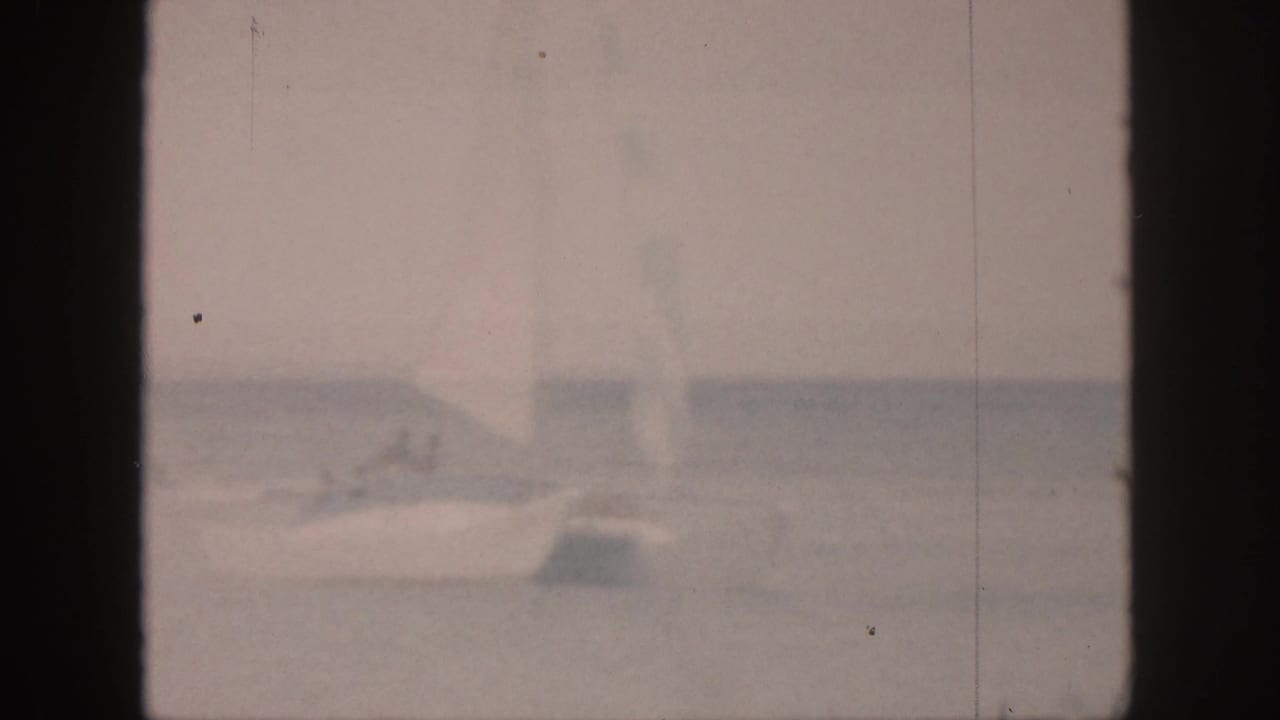 White sailboat with a raised sail moving across calm water.