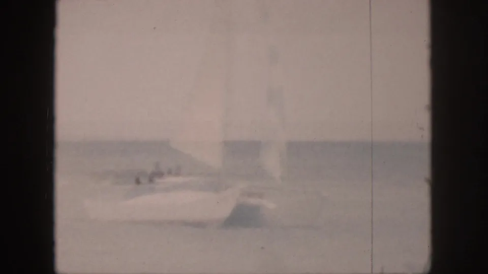 Soft 8mm view of a white sailboat in Hawaii, with indistinct passengers and a pale sail against the horizon.