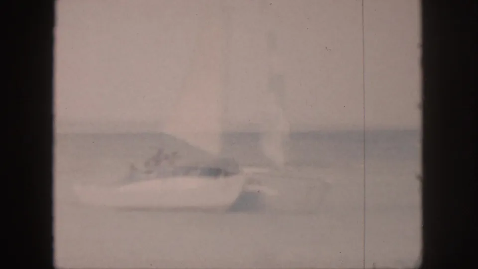 Faded 1959 Hawaii home-movie frame of a white sailboat crossing calm water, with small people visible aboard.