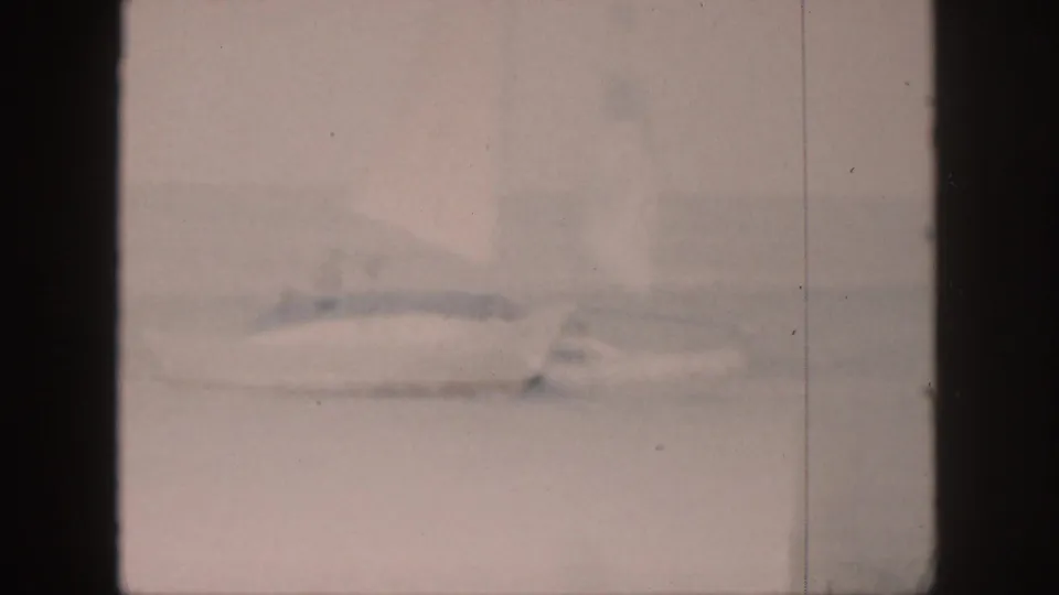Soft, faded 8mm frame from Hawaii showing a white sailboat with a raised sail and indistinct passengers on the water.