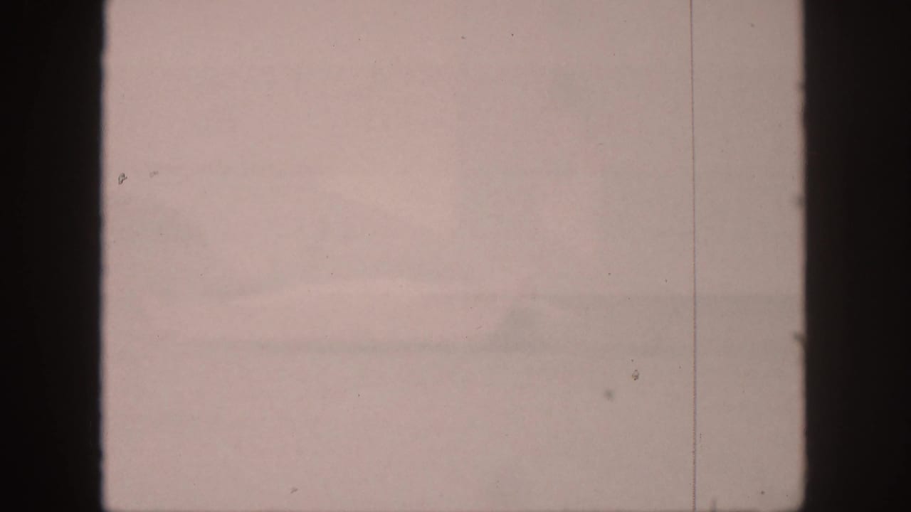 Hazy water and faint mountains seen through dark vertical film borders.