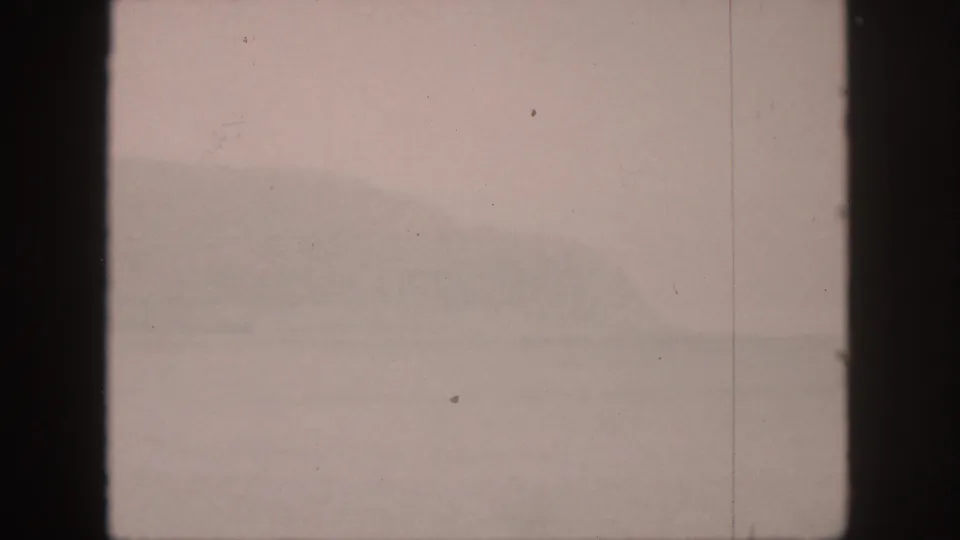 1959 Hawaii 8mm frame with blurred water, low mountain silhouettes, pinkish color shift, and visible film specks.