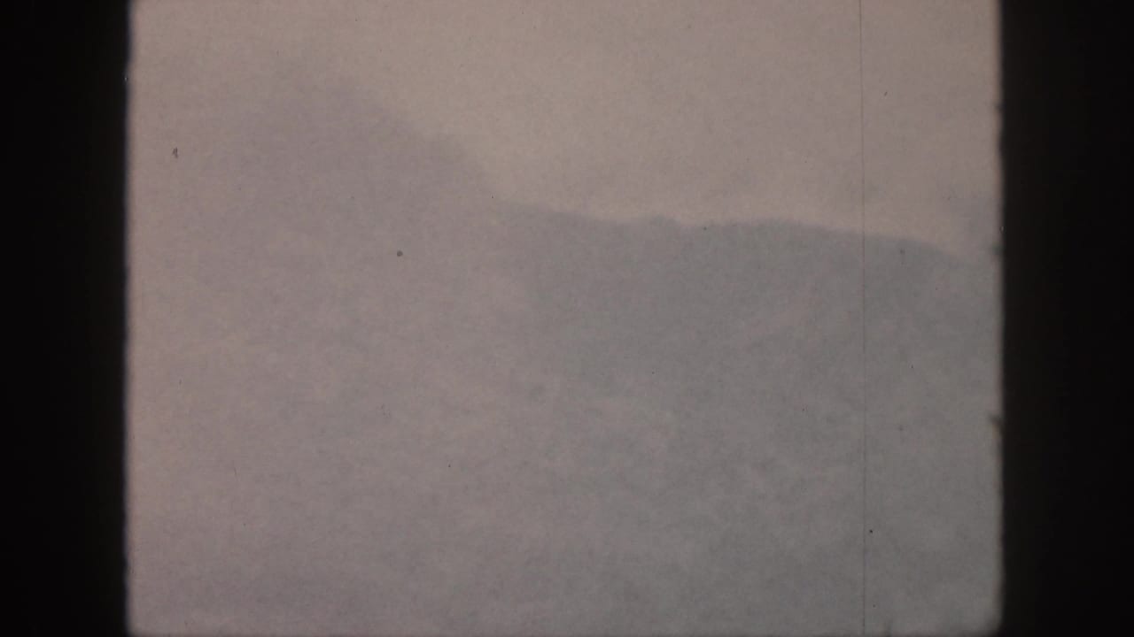 Hazy mountain ridge seen through dark vertical window bars under an overcast sky.