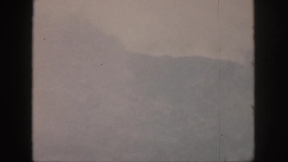 1959 Hawaii 8mm frame showing a fog-softened mountain ridge through dark vertical window bars, with muted color and film dust.