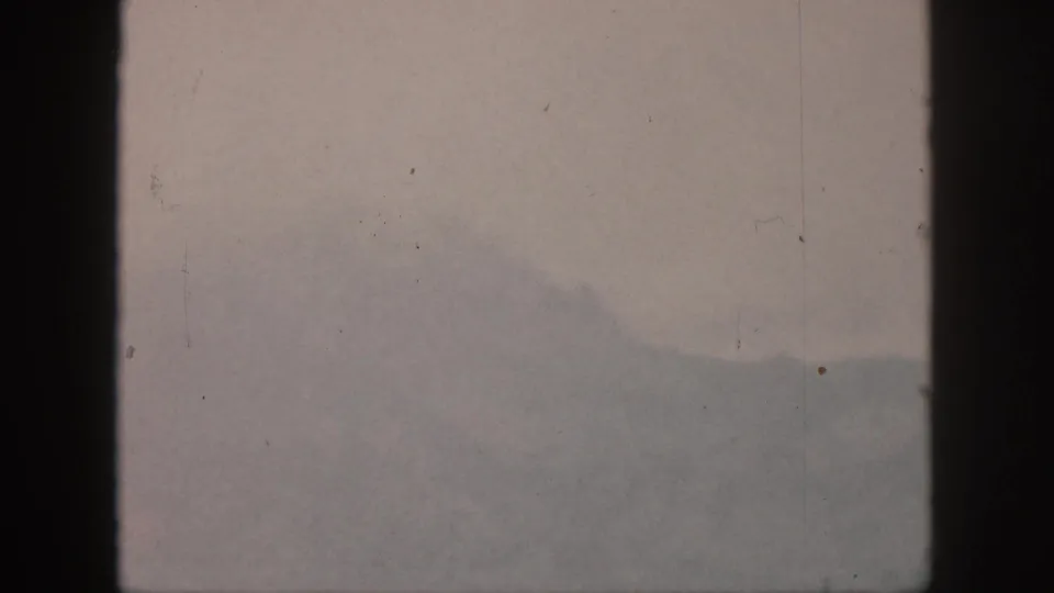 1959 Hawaii home-movie view of a distant mountain slope obscured by haze, divided by a dark vertical window or structural frame.
