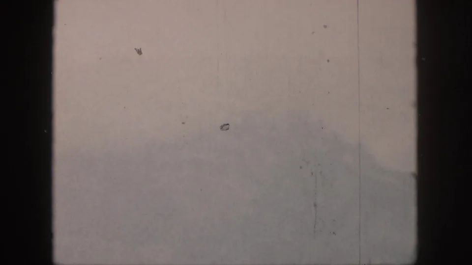 1959 Hawaii 8mm frame with low fog over a distant slope, seen through dark vertical bars and marked by dust and scratches.