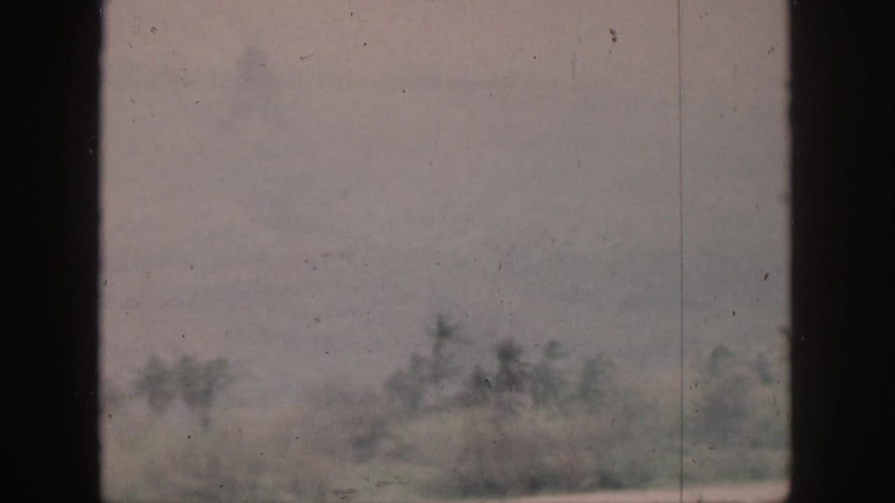 1959 Hawaii home-movie frame showing faint shoreline trees and haze through a dark window or structural frame.