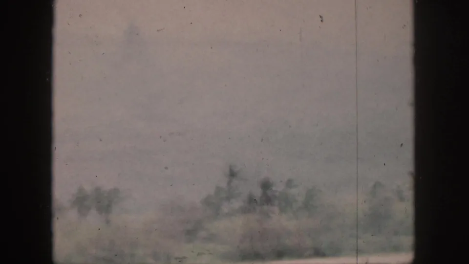 1959 Hawaii home-movie frame showing faint shoreline trees and haze through a dark window or structural frame.