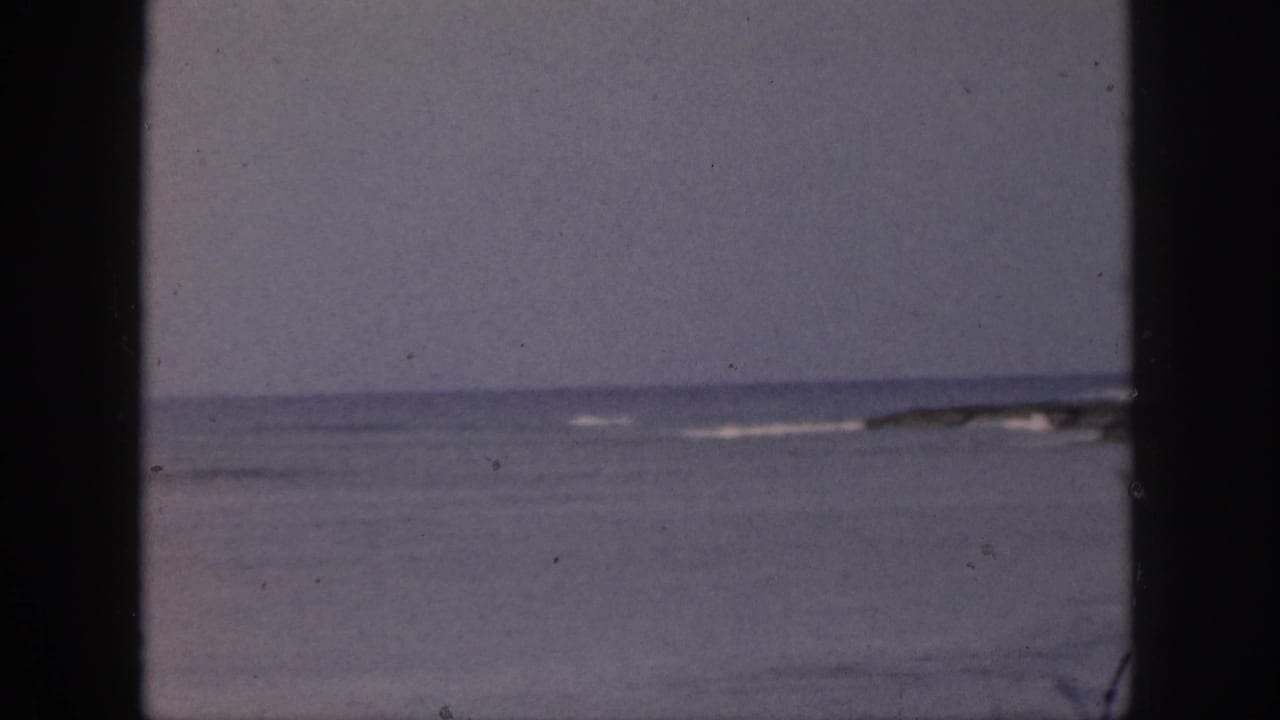 Ocean horizon seen through dark vertical window framing with faint surf in the distance.