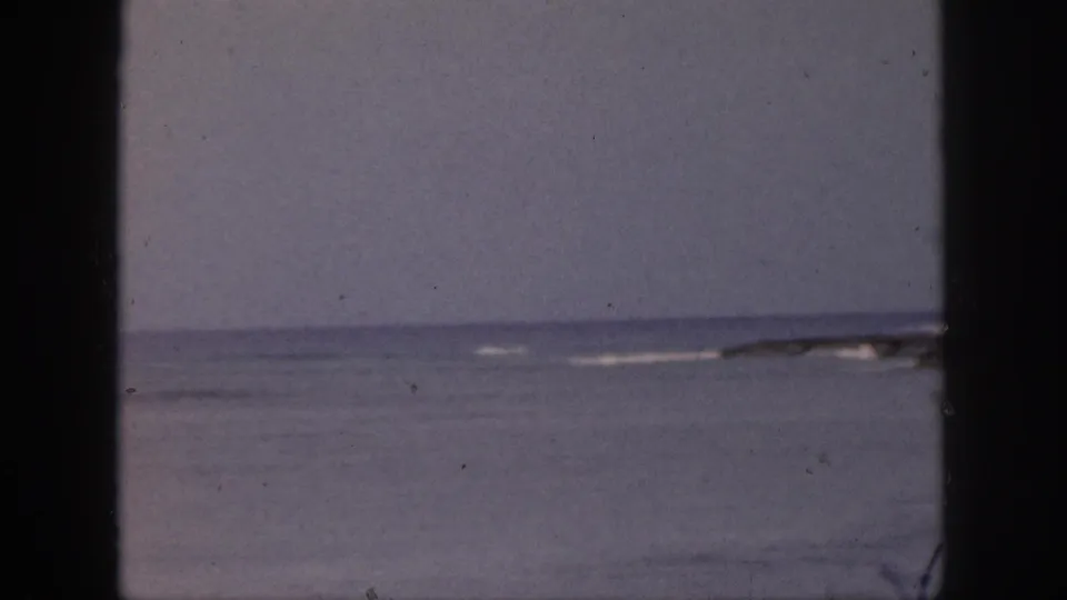 1959 Hawaii 8mm frame showing a soft ocean horizon through dark window framing, with faint surf and pale sky.
