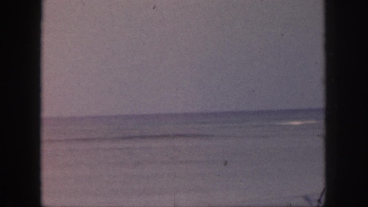 Distant waterline with small surf breaks, viewed between dark vertical frame edges.