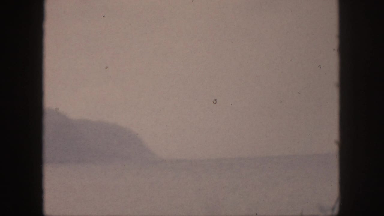 1959 Hawaii 8mm frame showing a distant mountain range across still water, with soft color and visible film specks.