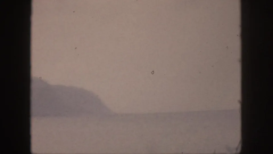 1959 Hawaii 8mm frame showing a distant mountain range across still water, with soft color and visible film specks.