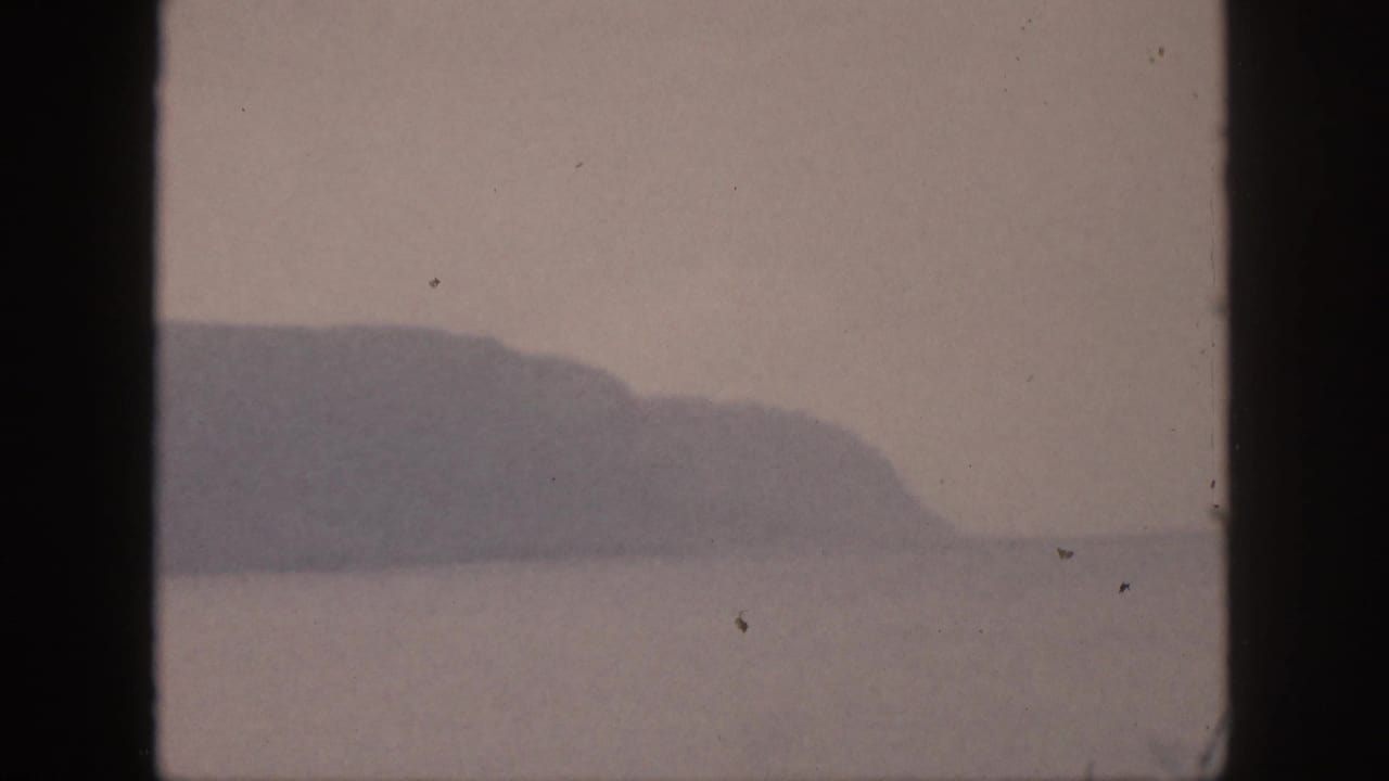 Distant headland or mountain slope above calm water, framed by film borders.