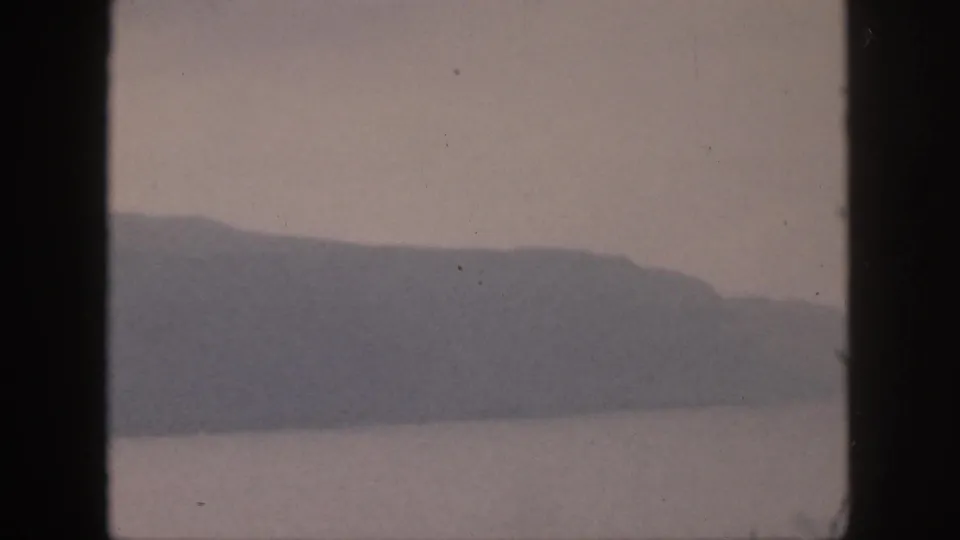 1959 Hawaii 8mm frame showing a low, distant mountain ridge across water, with muted color and home-movie softness.
