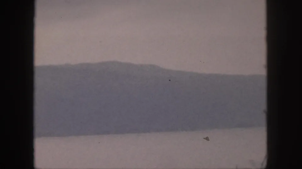 1959 Hawaii 8mm frame of a blue-gray mountain range across still water, with visible grain and light film wear.
