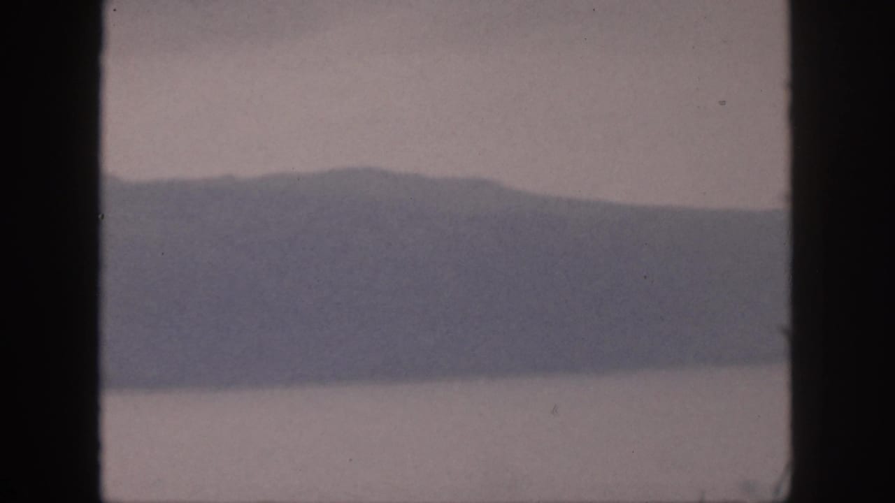 Hazy mountain ridge above calm water, seen through dark vertical window framing.