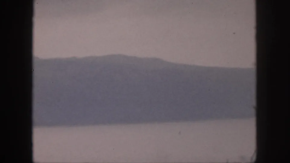 1959 Hawaii 8mm frame showing distant mountains above still water, partially framed by dark vertical window edges.