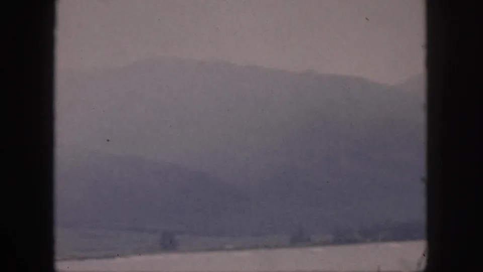1959 Hawaii 8mm still with layered mountain forms above water, softened by haze and framed by dark edges.