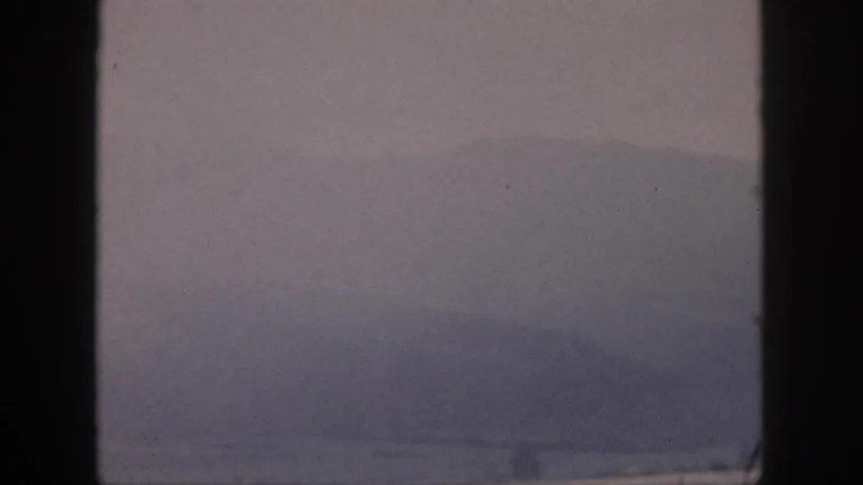 1959 Hawaii home-movie frame showing a faint mountain ridge beyond water, with dark foreground window framing.
