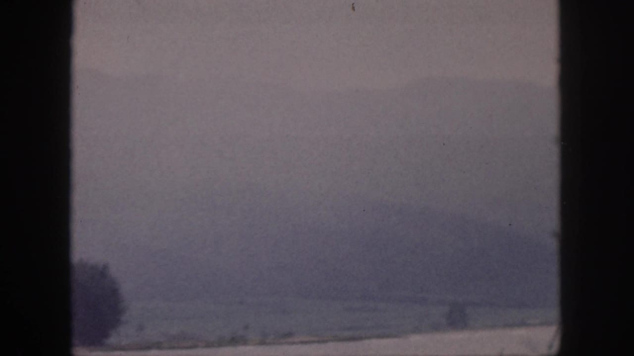 Hazy hills and distant landscape seen through dark vertical window framing.