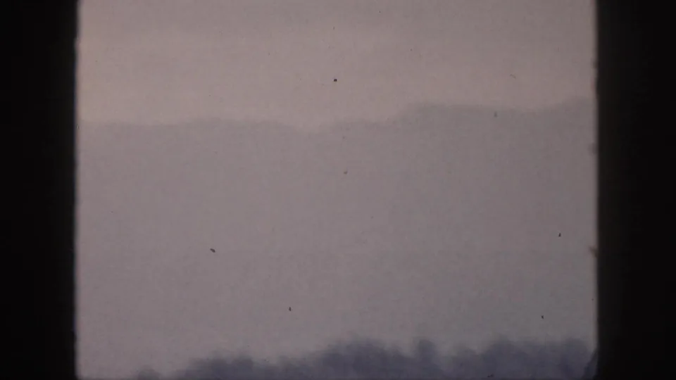 Muted 1959 Hawaii 8mm view of low hazy hills and dark foreground vegetation through a window-like frame.
