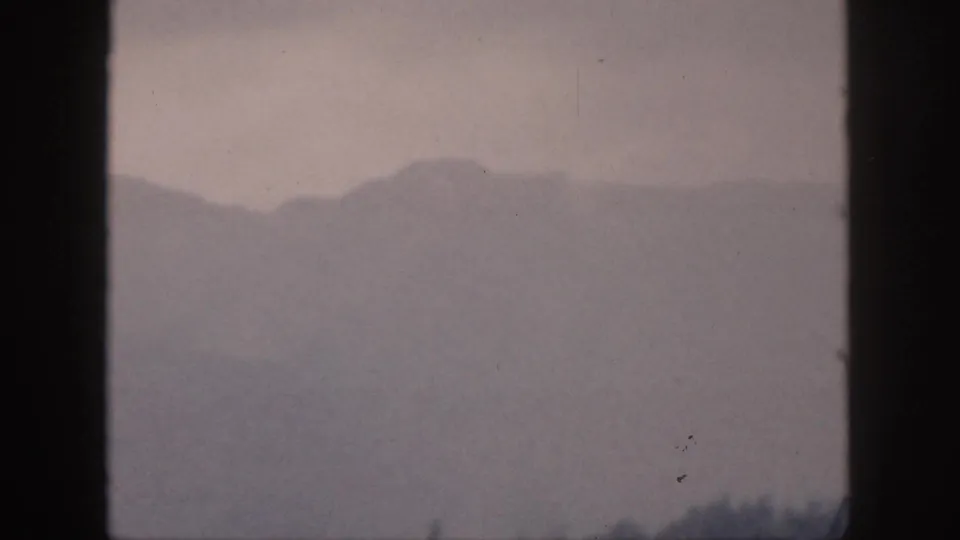 1959 Hawaii 8mm frame showing distant mountain shapes softened by mist, with dark frame bars and faint tree silhouettes.