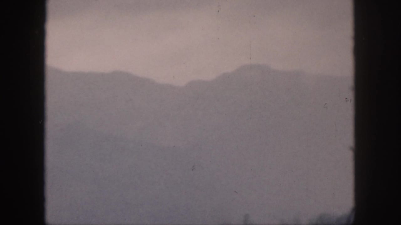 1959 Hawaii 8mm frame showing fog-softened mountain ridges through a dark window frame with muted gray-purple tones.