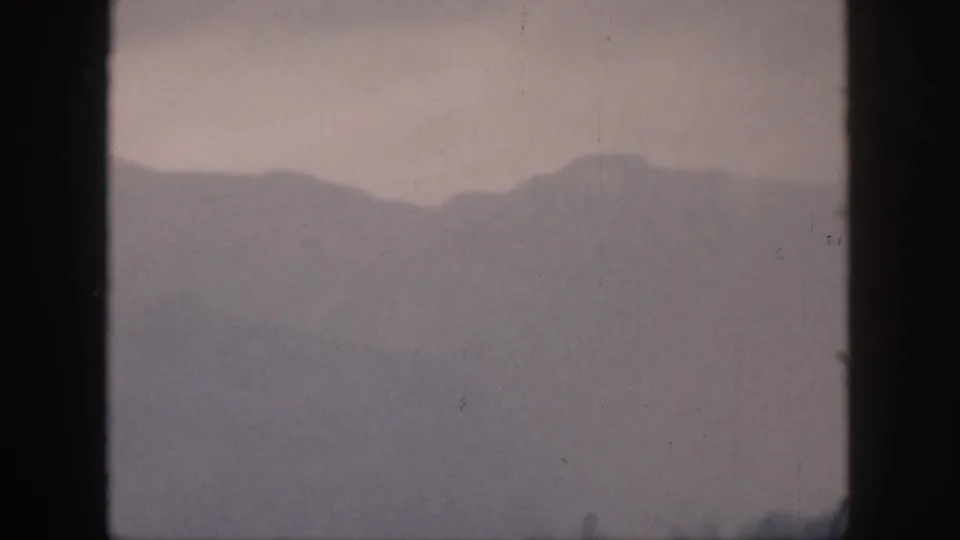 1959 Hawaii 8mm frame showing fog-softened mountain ridges through a dark window frame with muted gray-purple tones.