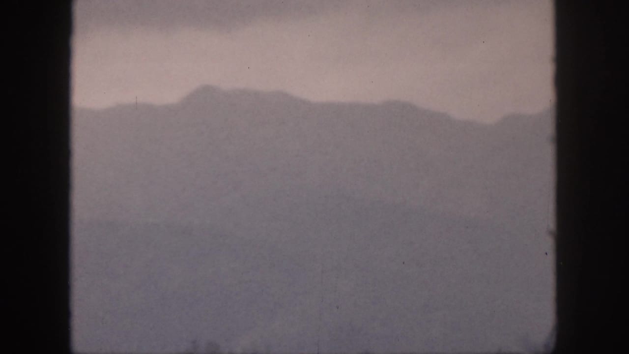 Distant mountain ridge framed by dark vertical window bars in hazy light.