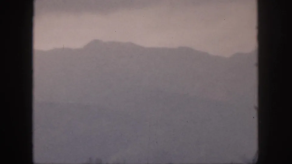 1959 Hawaii home-movie still with a distant misty mountain ridge viewed through dark window mullions.