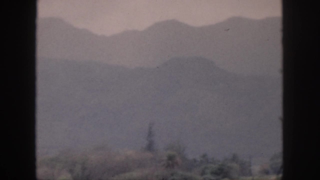 1959 Hawaii 8mm frame showing distant mountain ridges fading into mist beneath a cloudy sky, bordered by the film gate.