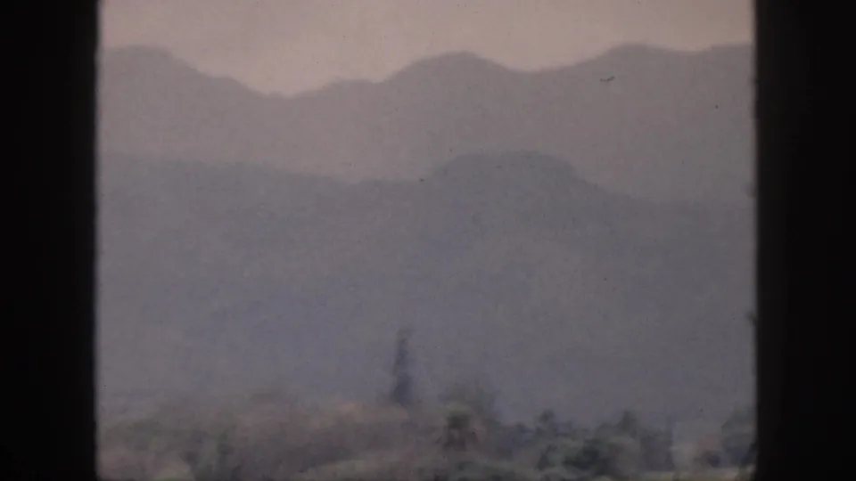 1959 Hawaii 8mm frame showing distant mountain ridges fading into mist beneath a cloudy sky, bordered by the film gate.