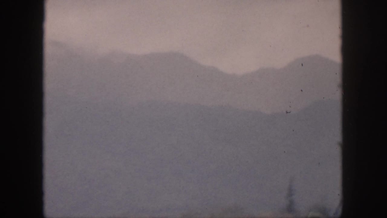 1959 Hawaii home-movie view of hazy mountain silhouettes and low clouds seen through dark 8mm frame edges.