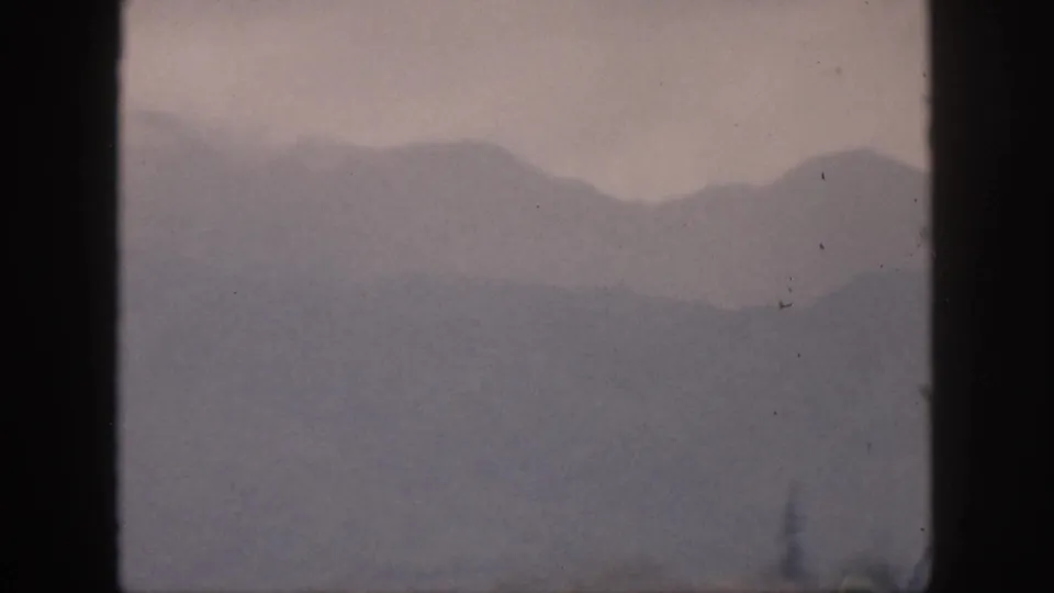 1959 Hawaii home-movie view of hazy mountain silhouettes and low clouds seen through dark 8mm frame edges.