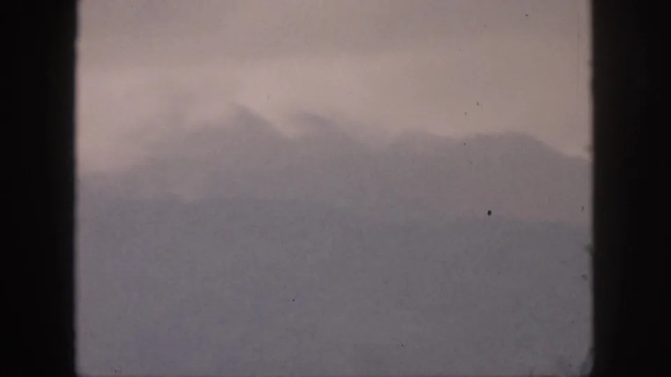 1959 Hawaii 8mm frame with a mountain ridge softened by mist and cloud, showing muted color and film wear.