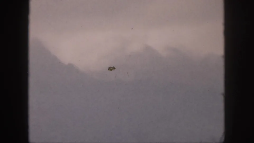 1959 Hawaii 8mm view of a mist-covered mountain slope under an overcast sky, with visible film dust and soft exposure.