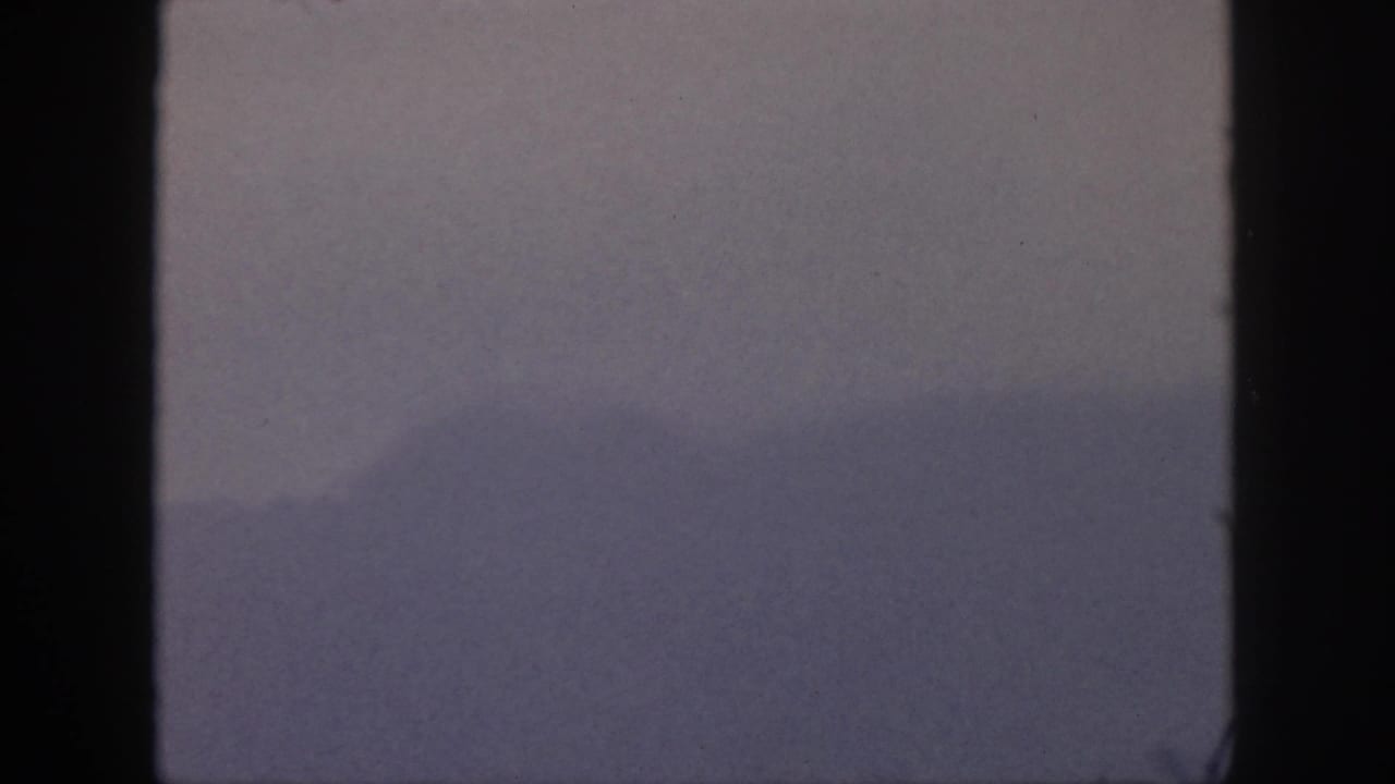 Hazy 1959 Hawaii landscape frame with subdued mountain forms and heavy dark edging from the film gate.