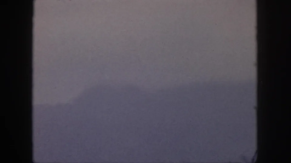 Hazy 1959 Hawaii landscape frame with subdued mountain forms and heavy dark edging from the film gate.