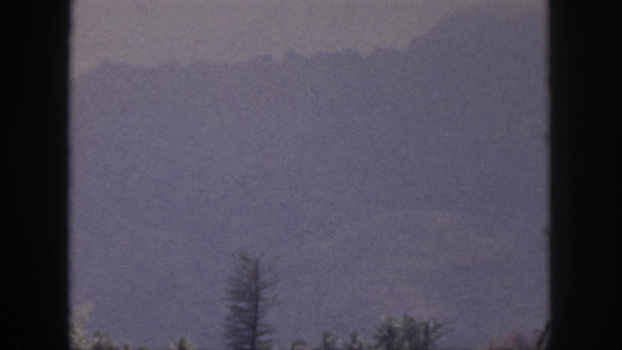 1959 Hawaii 8mm view of a misty mountain slope and sparse treetops through dark window-like framing.