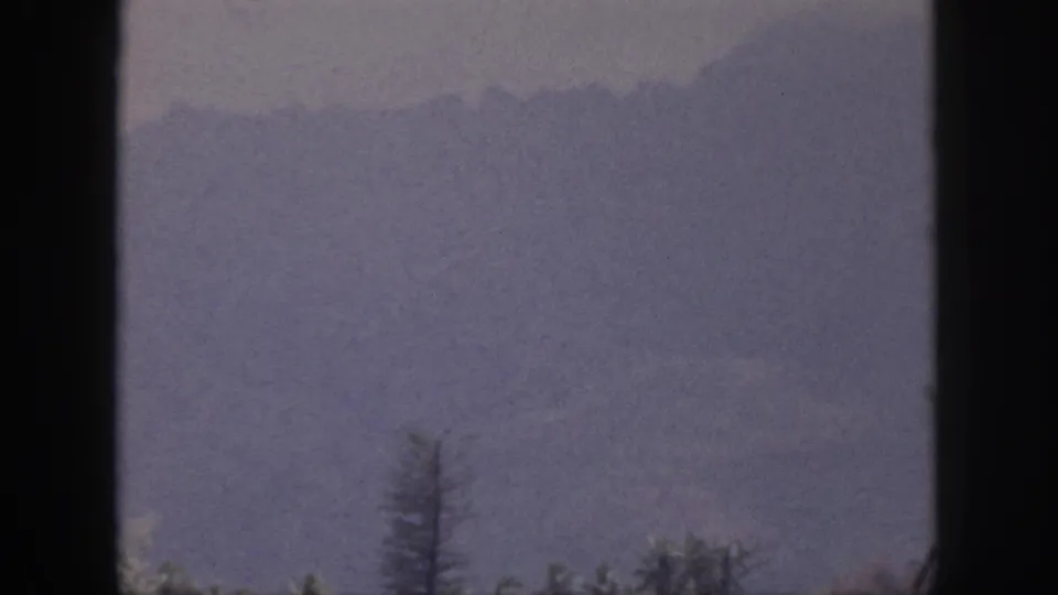1959 Hawaii 8mm view of a misty mountain slope and sparse treetops through dark window-like framing.