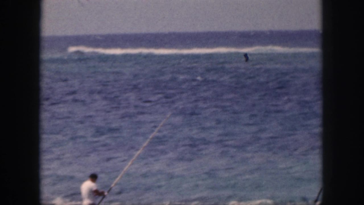 Man partly low in frame holding a fishing pole near the surf.