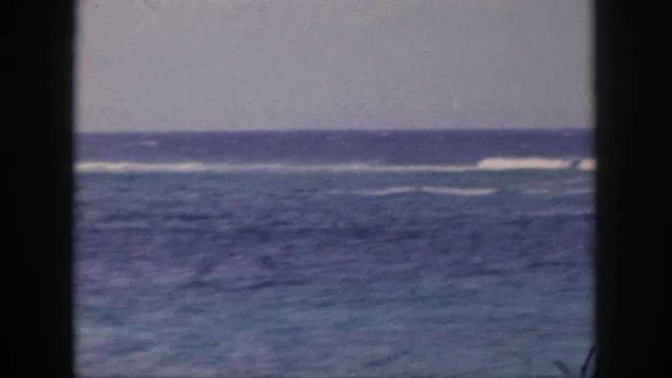 1959 Hawaii home-movie frame showing blue ocean, reef-like surf lines, and a partial fishing pole near the right edge.