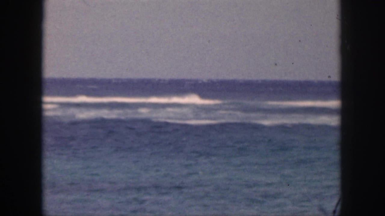 1959 Hawaii 8mm frame showing blue ocean surf and white wave lines viewed through a dark window or doorway frame.