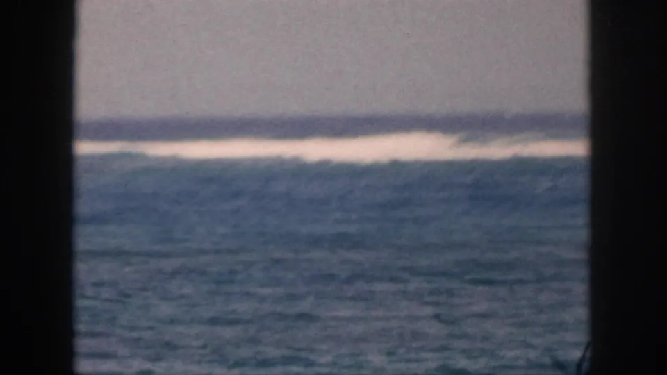 1959 Hawaii home-movie frame showing a soft ocean horizon and a broad band of white surf across blue water.