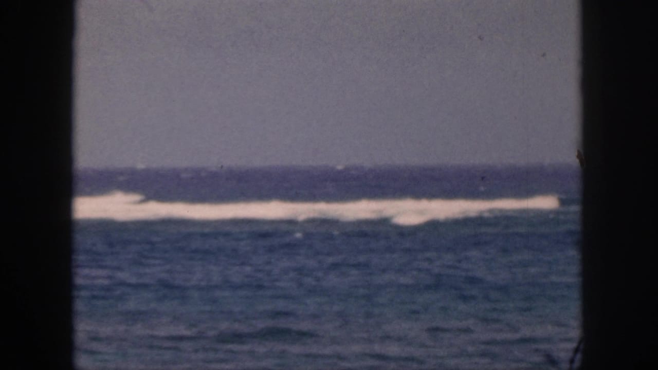 1959 Hawaii 8mm still with distant white breakers, blue water, overcast sky, and a dark foreground divider.
