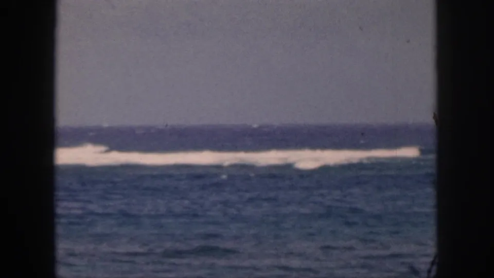 1959 Hawaii 8mm still with distant white breakers, blue water, overcast sky, and a dark foreground divider.